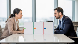 Une salariée et un conseiller en ressources humaines comparent des dossiers vierges autour d’une table dans un bureau lumineux.