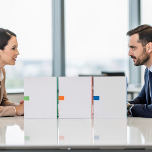 Une salariée et un conseiller en ressources humaines comparent des dossiers vierges autour d’une table dans un bureau lumineux.